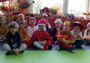 Grupka dzieci siedząca na tle kącika jesieni.